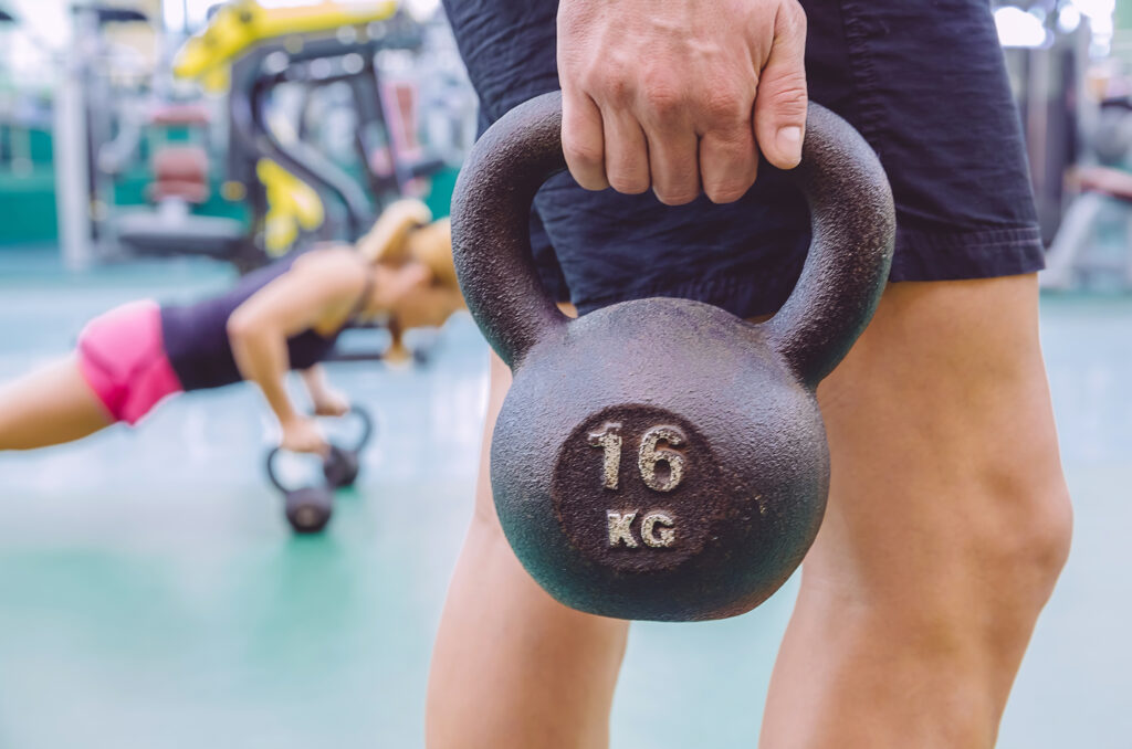 Closeup of athletic man holding black iron kettlebell and woman doing pushups over kettlebells in a crossfit training